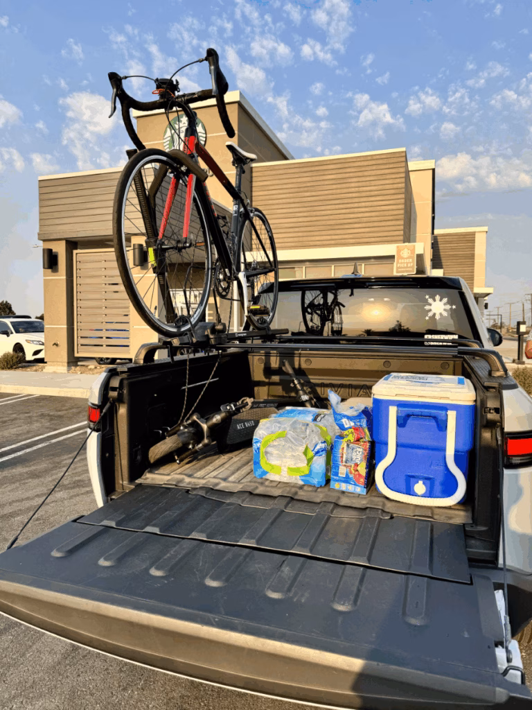 Rivian R1T with the bed open showing what's inside is an electric scooter, cooler, water, and rack with bicycle.