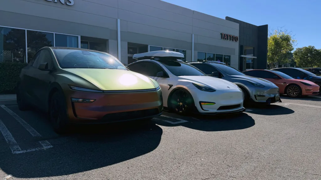 Unique iridescent car and several Teslas, including a white Model Y, parked in a sunny lot.