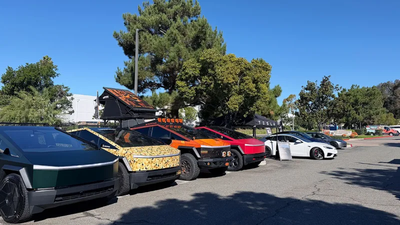 A line of customized Tesla Cybertrucks and other Teslas parked outdoors under a blue sky.