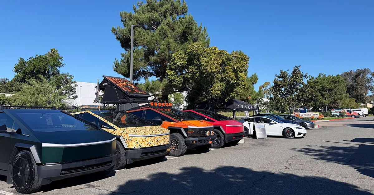 A line of customized Tesla Cybertrucks and other Teslas parked outdoors under a blue sky.